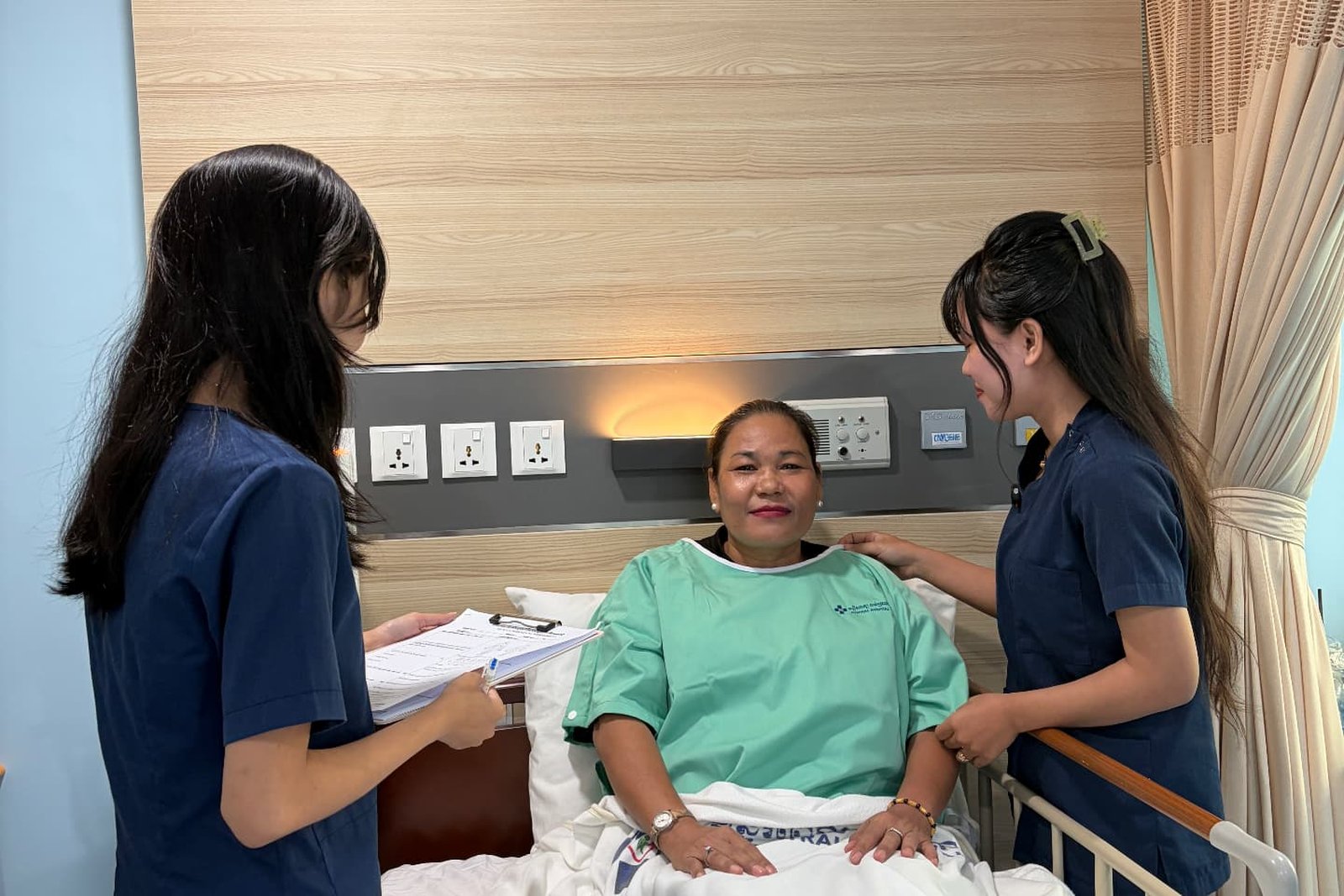 Two Metta Lotus caregivers in navy uniform attending to a patient resting comfortably in bed